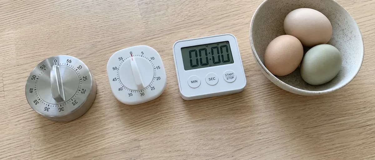 Tre kökstimers ovanifrån på en träbänk bredvid en skål med ägg