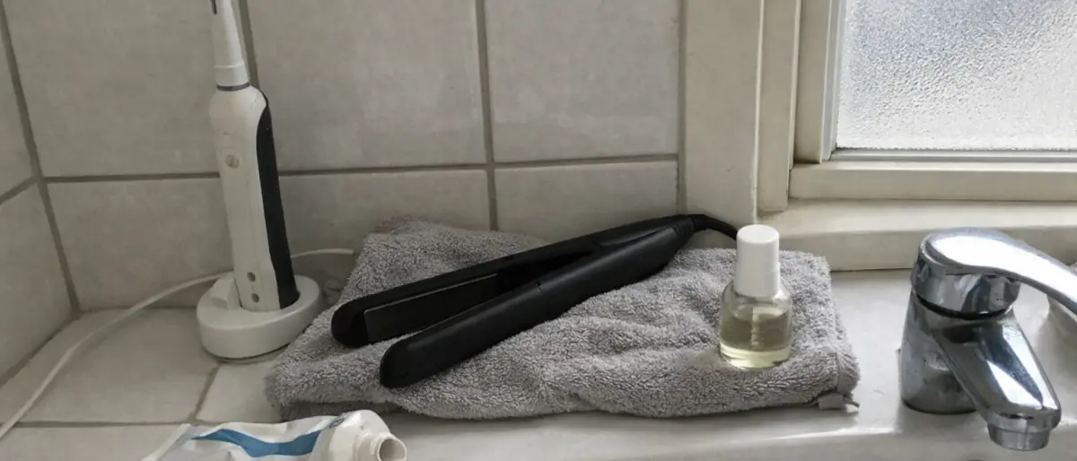 Badrumshylla med eltandborste i laddställ, plattång på handduk och nagelbehandling vid handfatet