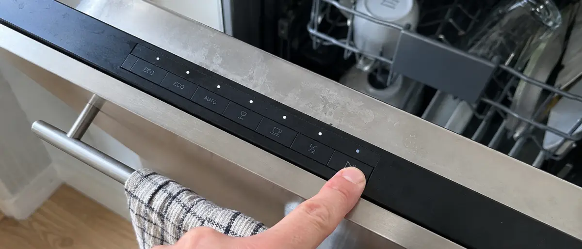 Närbild på ett finger som trycker på startknappen på en diskmaskins kontrollpanel ovanför luckan