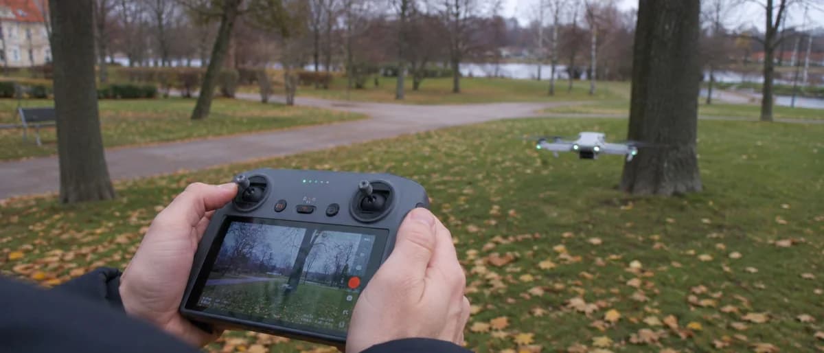 Person styr en drönare med fjärrkontroll och live-bild i en svensk park