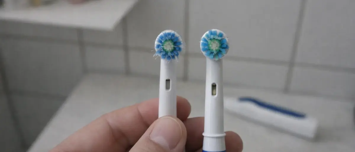 Hand som jämför två borsthuvuden till eltandborste i ett badrum