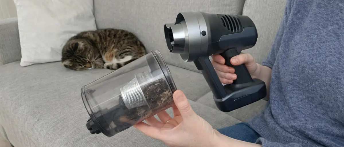 Person som kontrollerar dammbehållaren på en sladdlös dammsugare i en svensk lägenhet