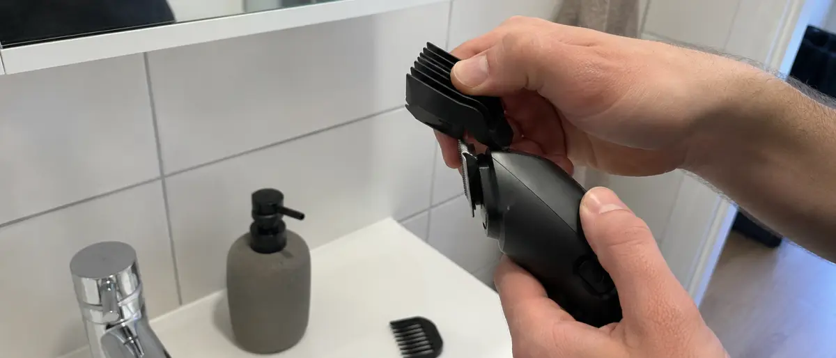 Händer som klickar fast ett kamtillbehör på hårtrimmerns trimhuvud över badrumshandfatet