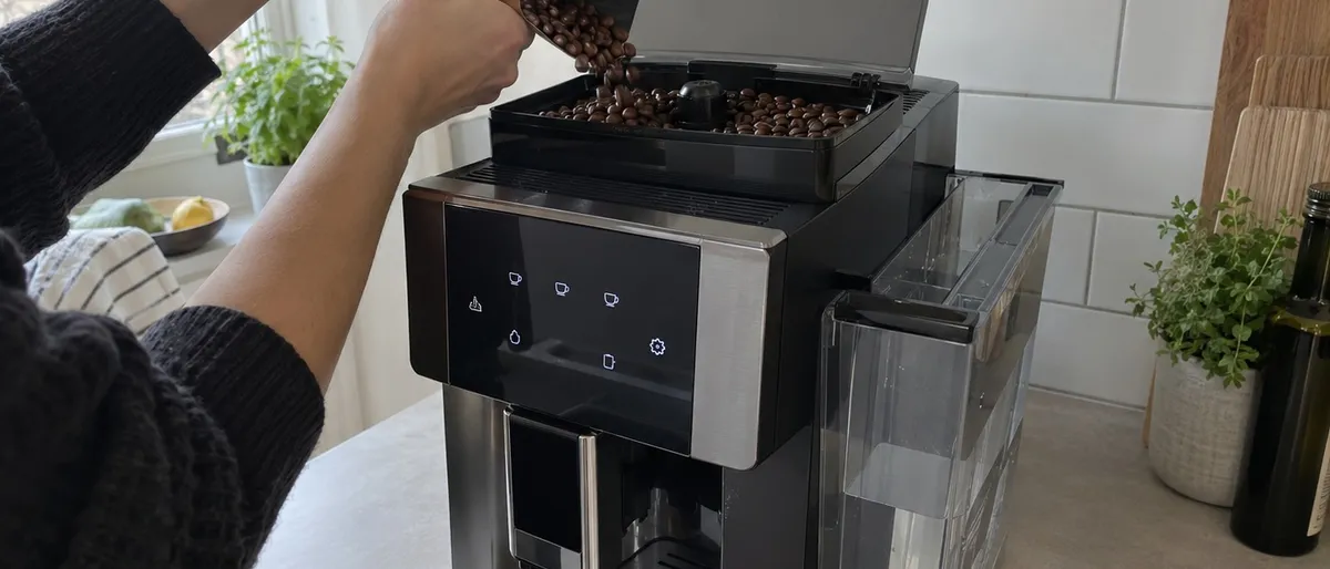 Person häller hela kaffebönor i bönbehållaren ovanpå en helautomatisk espressomaskin