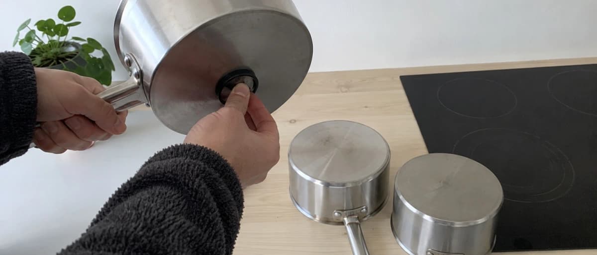 En magnet hålls mot undersidan av en rostfri kastrull för att kontrollera om den fungerar på induktionshäll