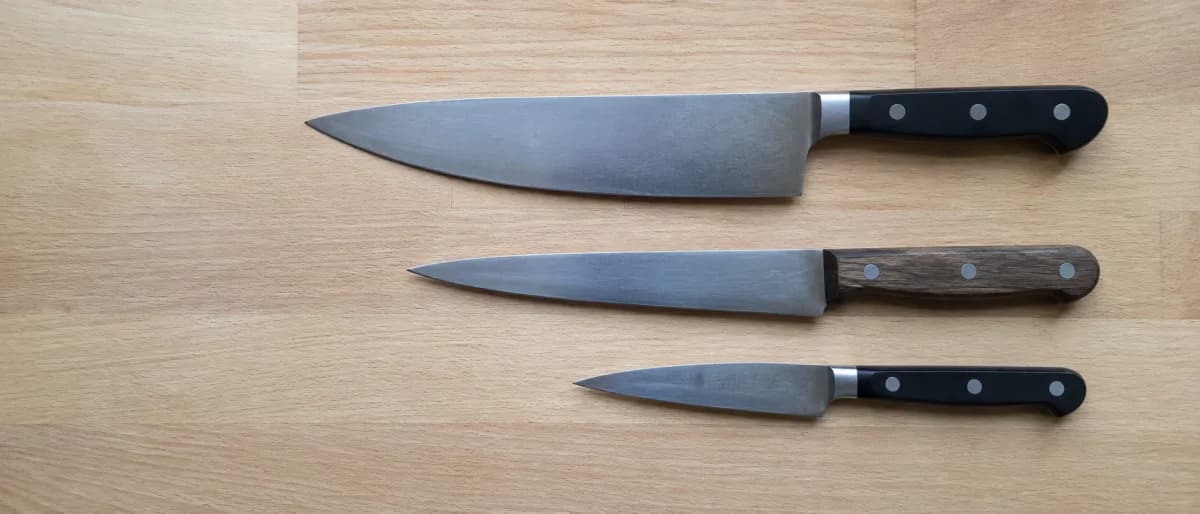 Tre kockknivar uppifrån på en ljus skärbräda i trä