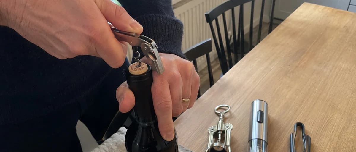 Händer som skruvar in spiralen på en kyparkorkskruv i korken, med vingkorkskruv, elektrisk korkskruv och tvåbladig korkdragare bredvid