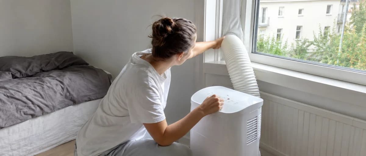 Person som monterar utblåsslangen till en portabel AC i ett fönster i ett sovrum
