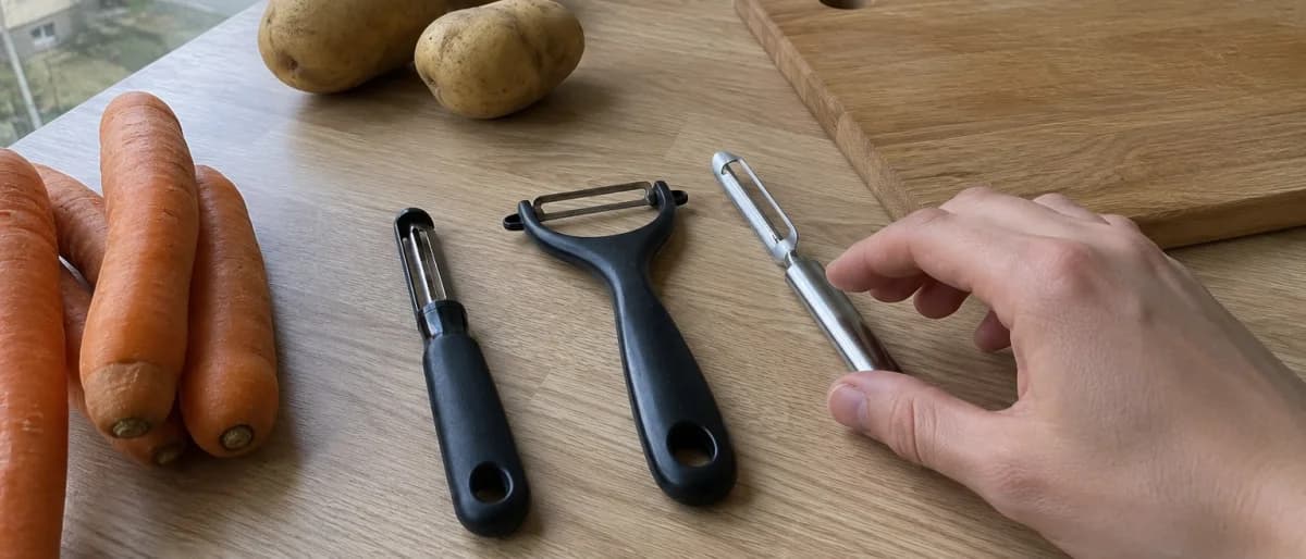Rak skalare, Y-skalare och stålskalare uppradade på en köksbänk med morötter och potatis intill