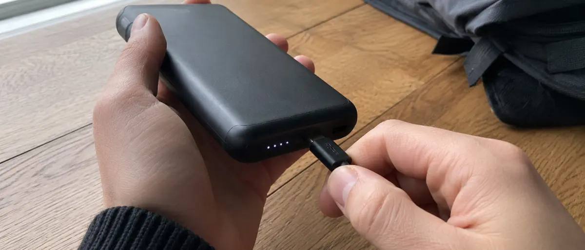 Händer som ansluter en USB-C-kabel i en svart powerbank med tänd LED-indikator