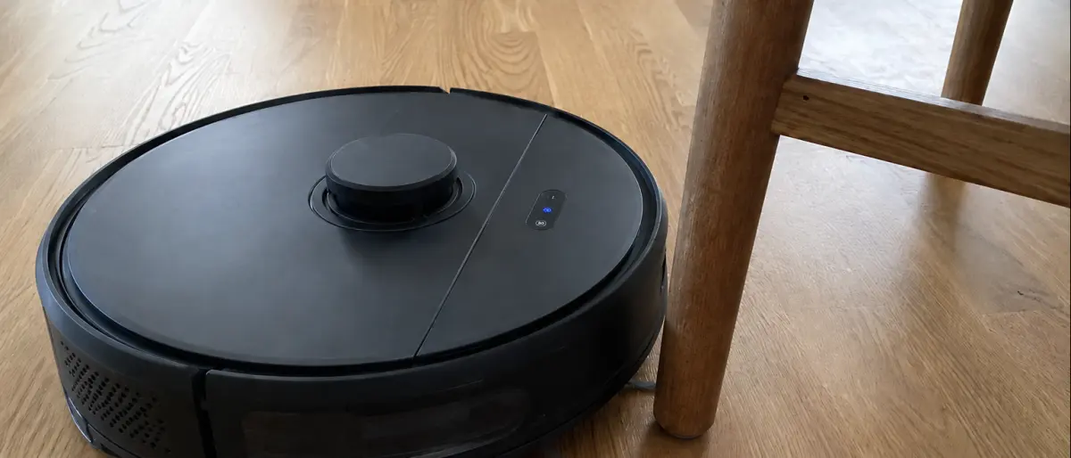 Närbild på svart robotdammsugare som navigerar runt stolsben på ekparkett