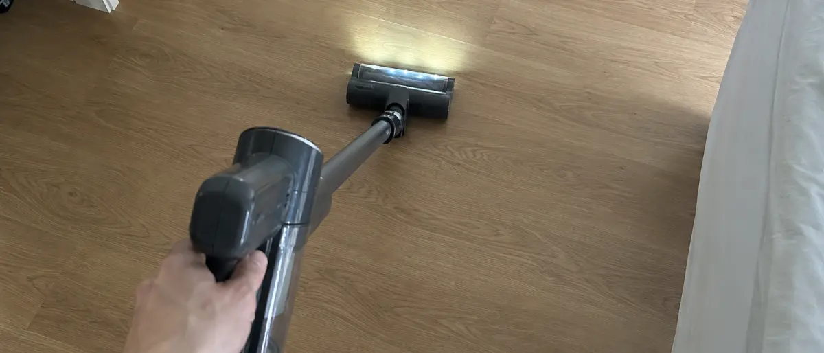 Hand som drar skaftdammsugaren över ekparketten med LED-lampan tänd