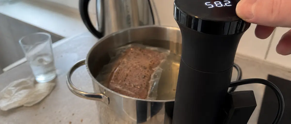 Närbild på en sous vide-cirkulators display med fingrar som ställer in temperaturen