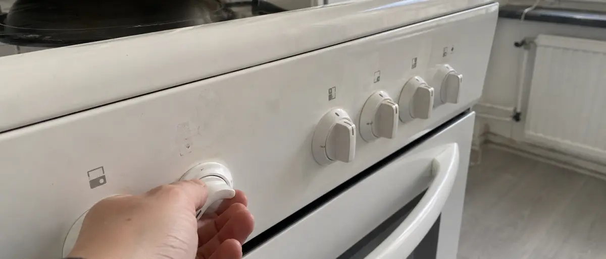 Närbild på en hand som vrider på en av spisens vred på den vita fronten