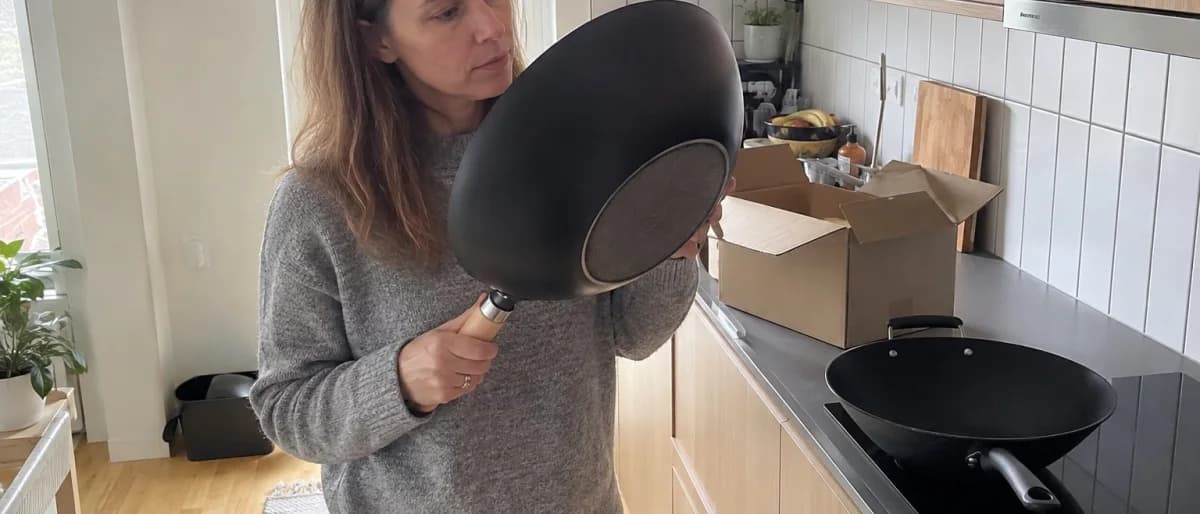 Kvinna i ett svenskt kök håller en ny wokpanna upp och ned och granskar den plana botten